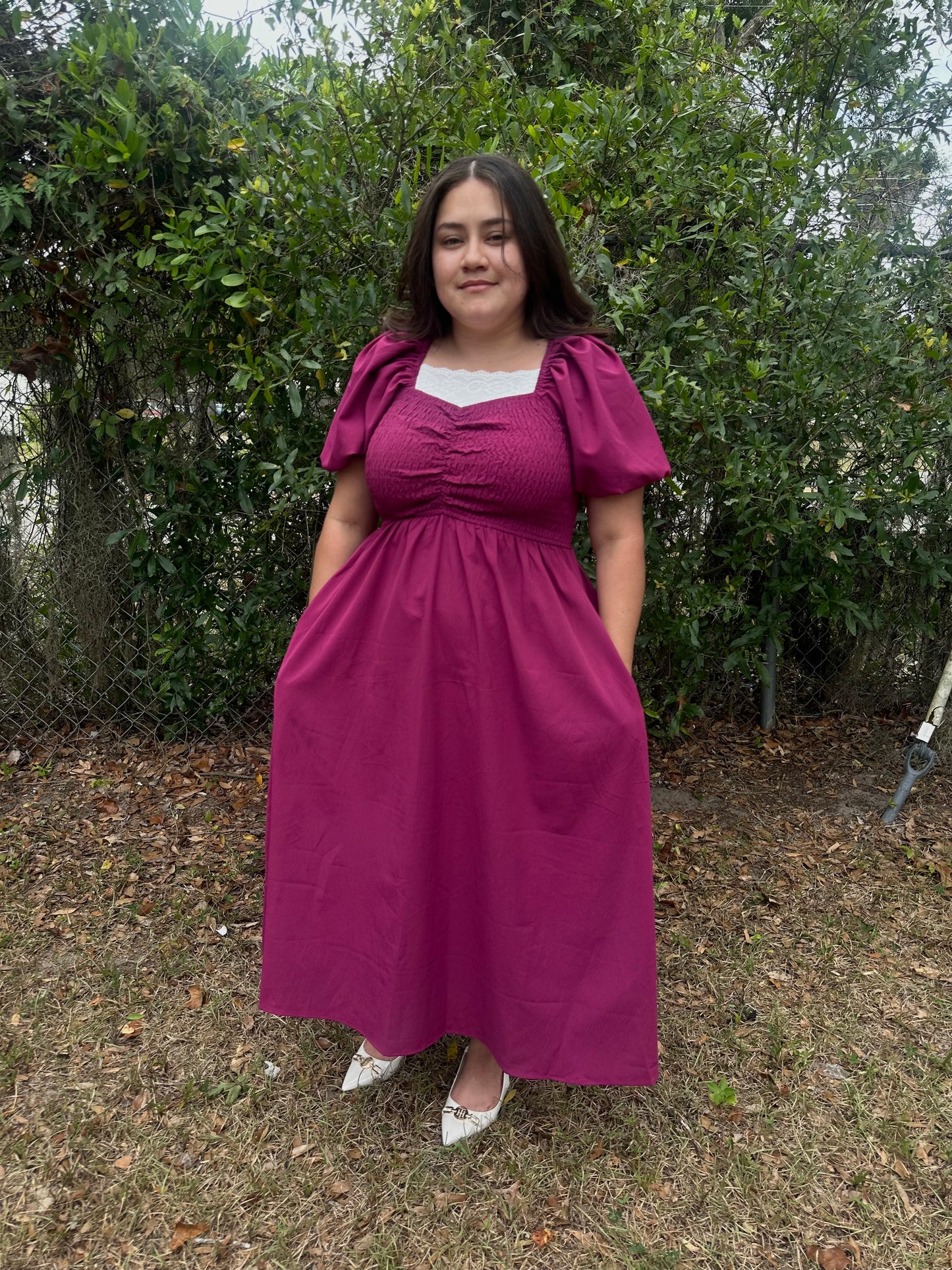 Woman wearing a magenta dress standing outdoors with greenery in the background