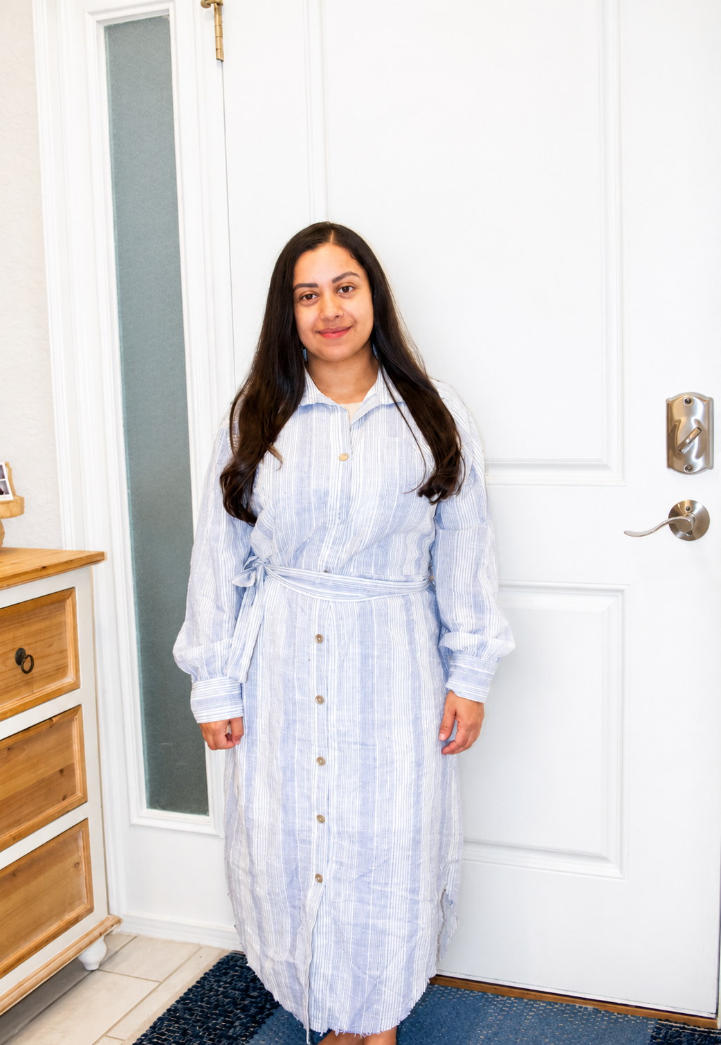 Woman wearing a blue and white striped dress standing in front of a white door.