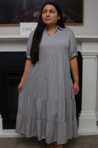 Woman wearing a gray tiered dress standing in a room with a fireplace.