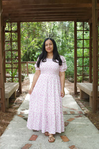 Woman in a pink dress standing under a wooden arbor with greenery in the background